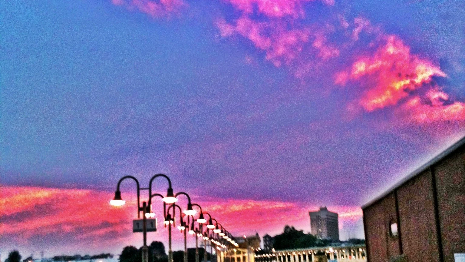Sunset over downtown Greensboro — a row of glowing platform lamps under a pink evening sky